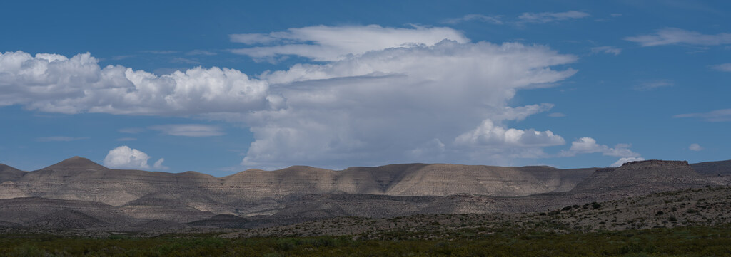 Low desert hills beneath a bank of cumulus clouds