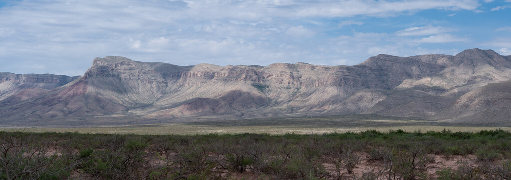 Mountain escarpment across desert scrub under high clouds