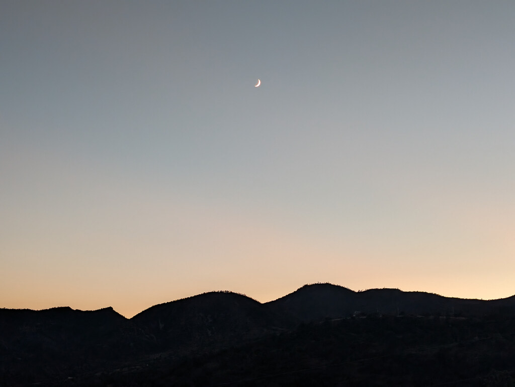 Crescent moon over dark rounded hills