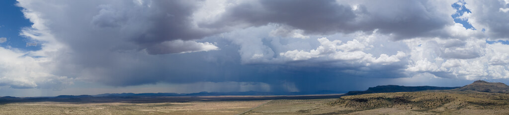 Rain shaft below dark storm clouds above distant mesas