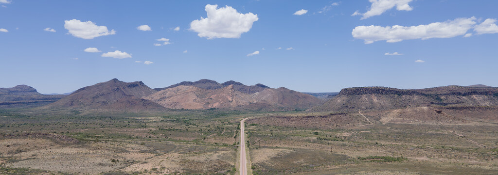 Aerial view along a straight road toward red desert mountains