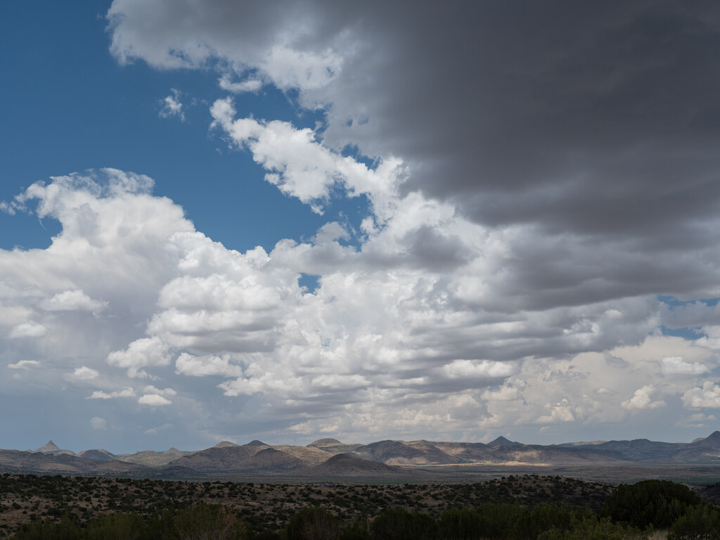 Cumulus clouds over low mountains and a dark foreground ridge
