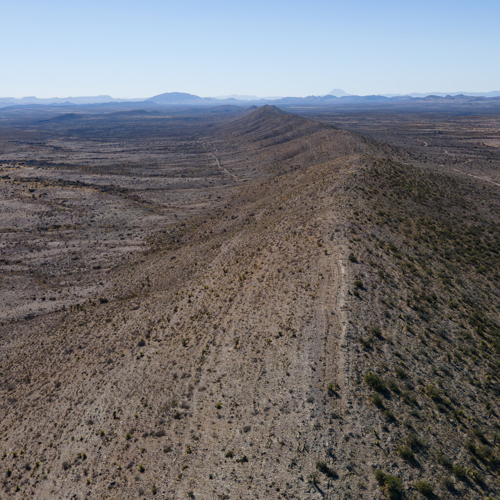 Aerial view down a desert ridge toward distant mountains