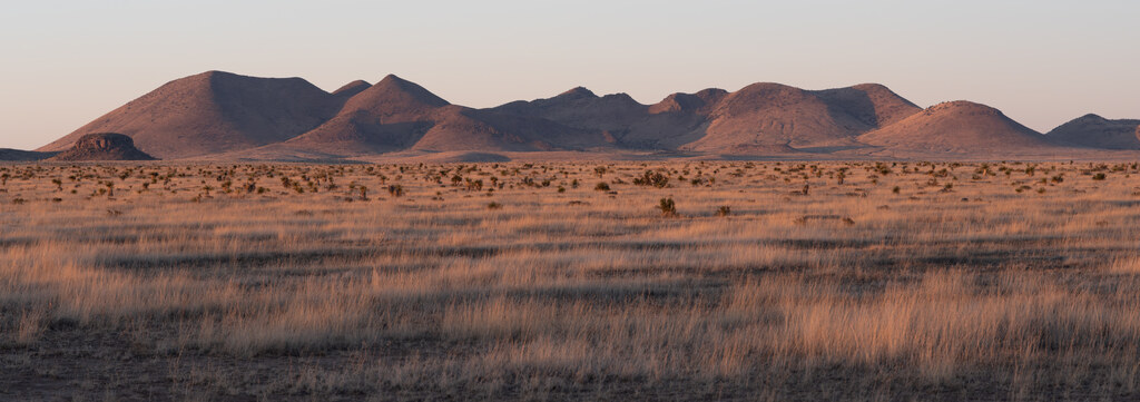 Low mountains in pink evening light beyond dry grassland