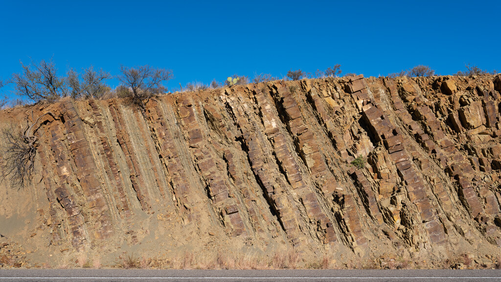 Steep rust-colored rock strata in a roadside cut