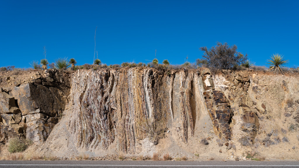 Roadcut exposing vertical folded rock beneath a clear blue sky